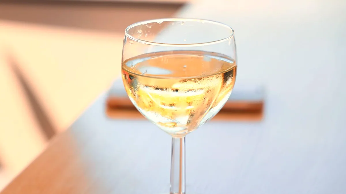 Una copa estrecha con vino blanco pálido a contraluz.