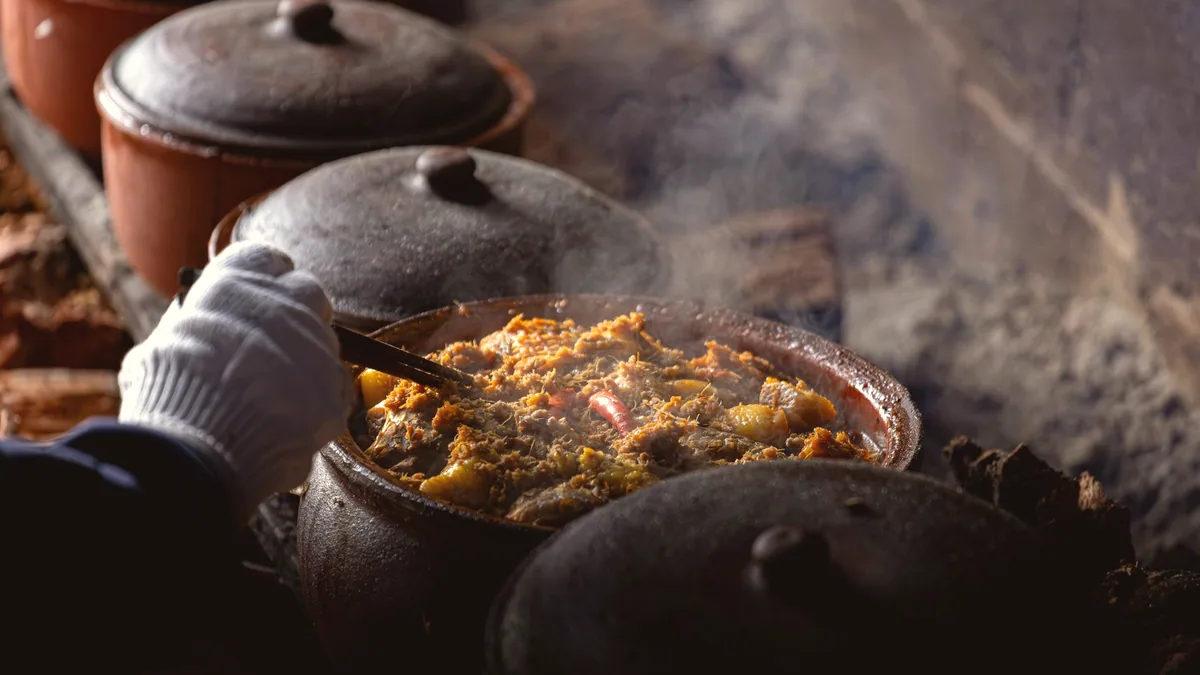 Una olla de barro al fuego con un guiso dentro.